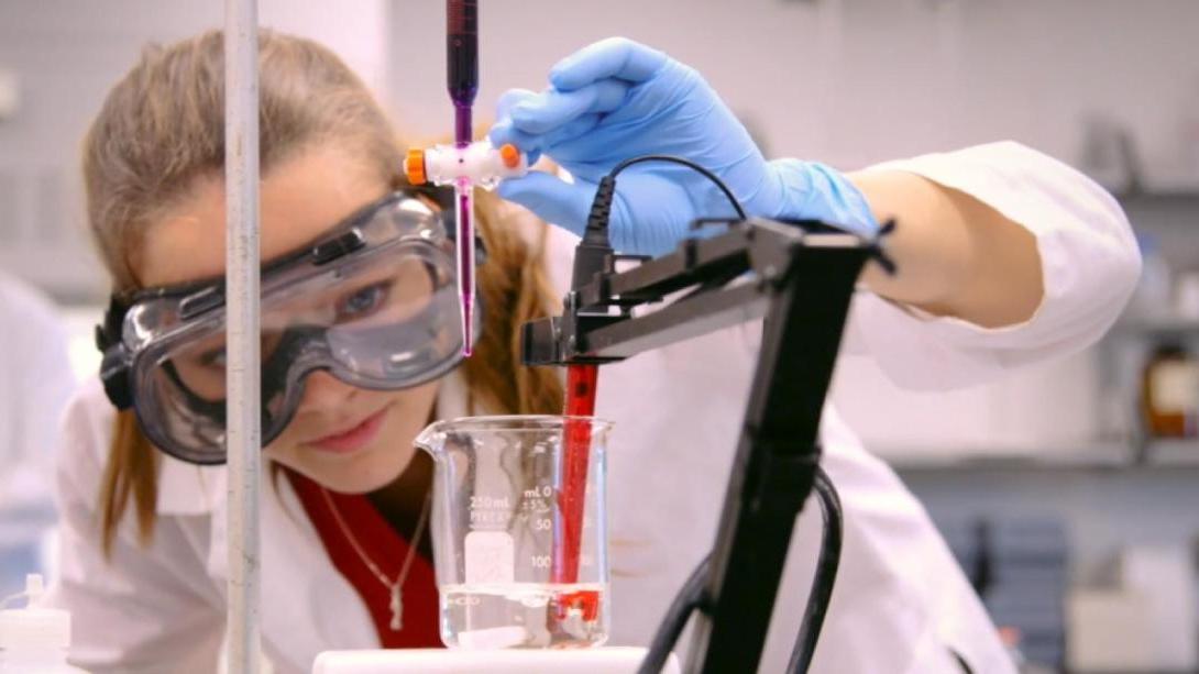 A student in a lab coat and goggles conducts a science experiment